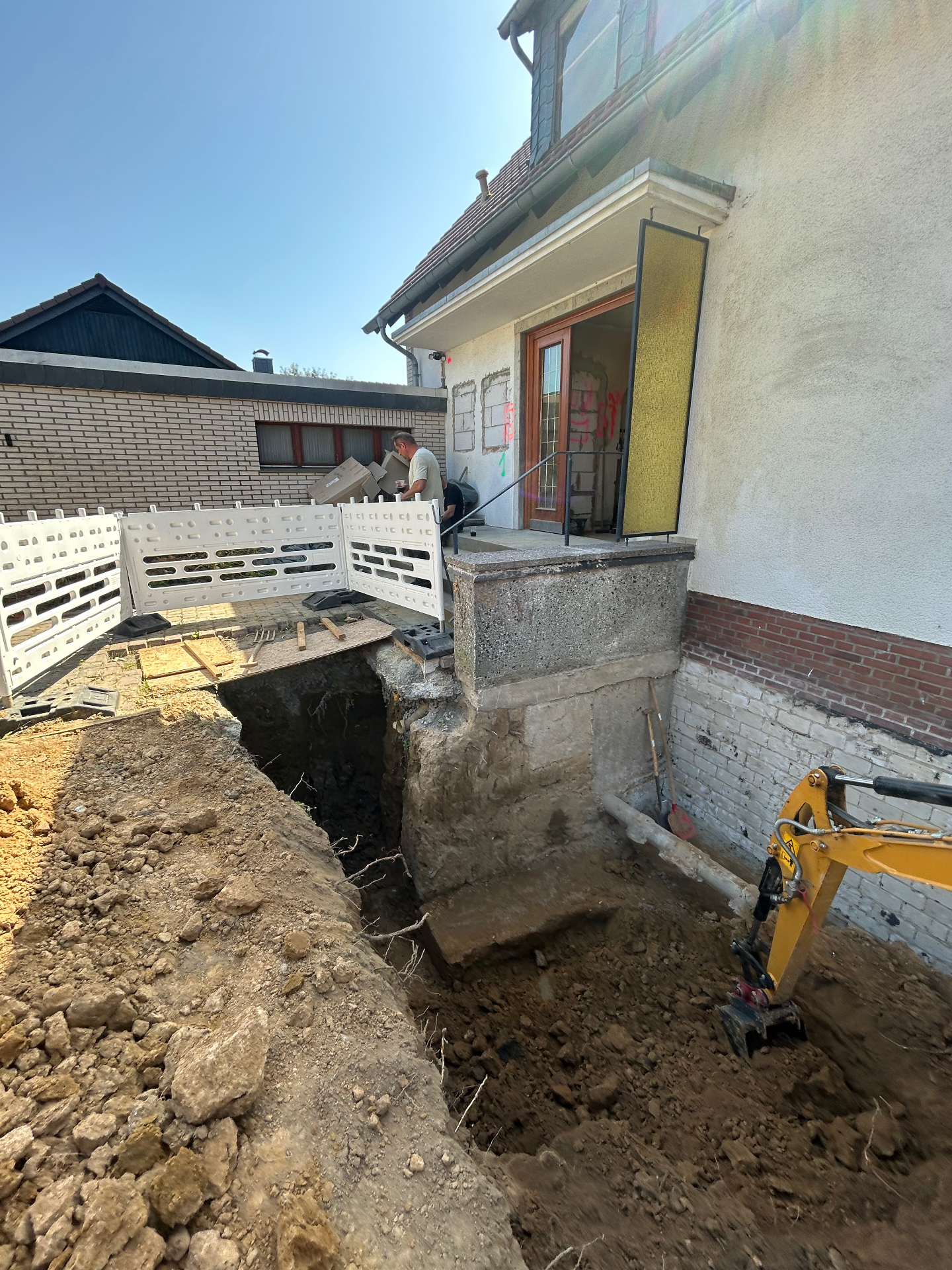 Aushub an einem Hauseingang mit freigelegtem Fundament und Bagger